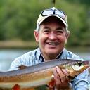 湖畔で大きな魚を誇らしげに持つ鈴木様 (54歳)